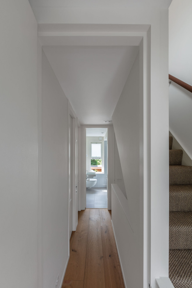 Photo of a small contemporary hallway in London with white walls, light hardwood floors, brown floor and recessed.