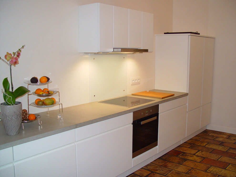 This is an example of a mid-sized contemporary eat-in kitchen in Frankfurt with concrete benchtops, white splashback, glass sheet splashback, stainless steel appliances and terra-cotta floors.