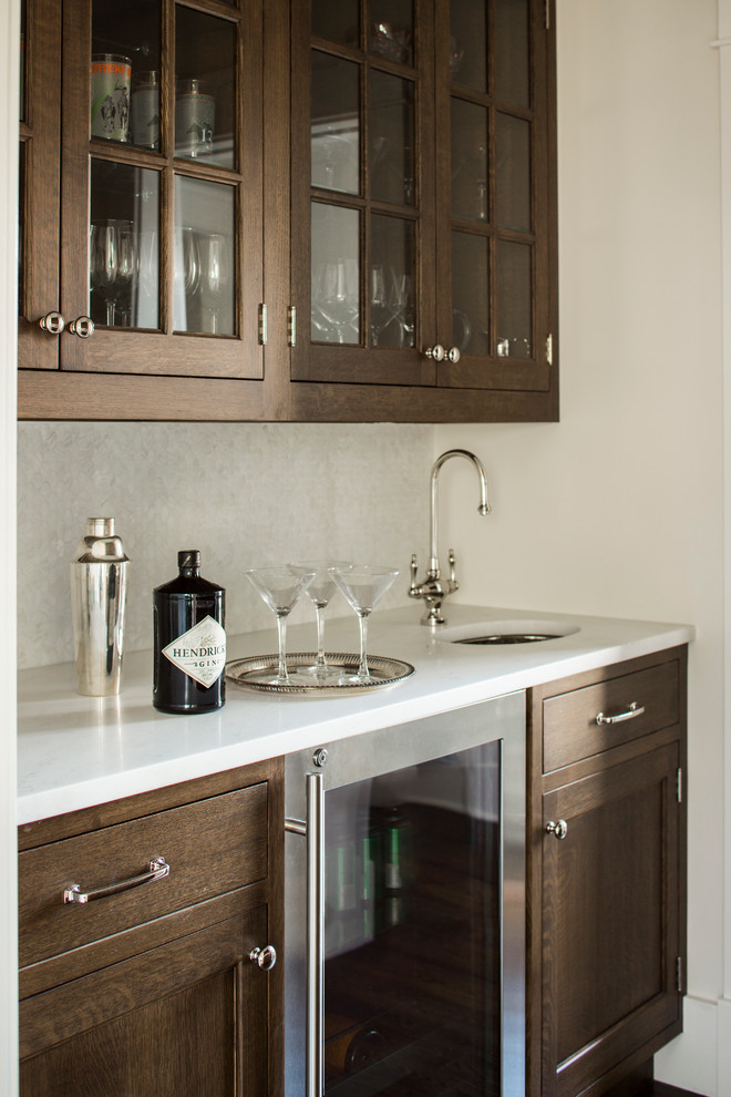 This is an example of a large traditional galley wet bar in New York with an undermount sink, shaker cabinets, medium wood cabinets, marble benchtops, beige splashback, mosaic tile splashback and white benchtop.