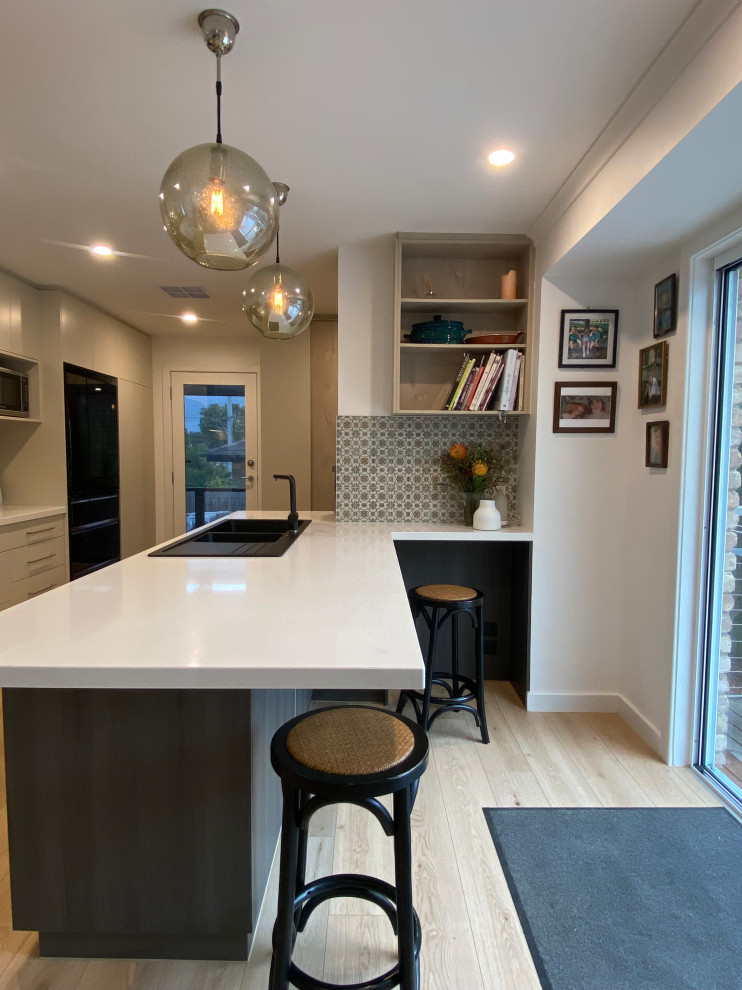This is an example of a mid-sized transitional galley eat-in kitchen in Melbourne with a double-bowl sink, flat-panel cabinets, green cabinets, quartz benchtops, grey splashback, mirror splashback, black appliances, laminate floors, a peninsula, brown floor and white benchtop.