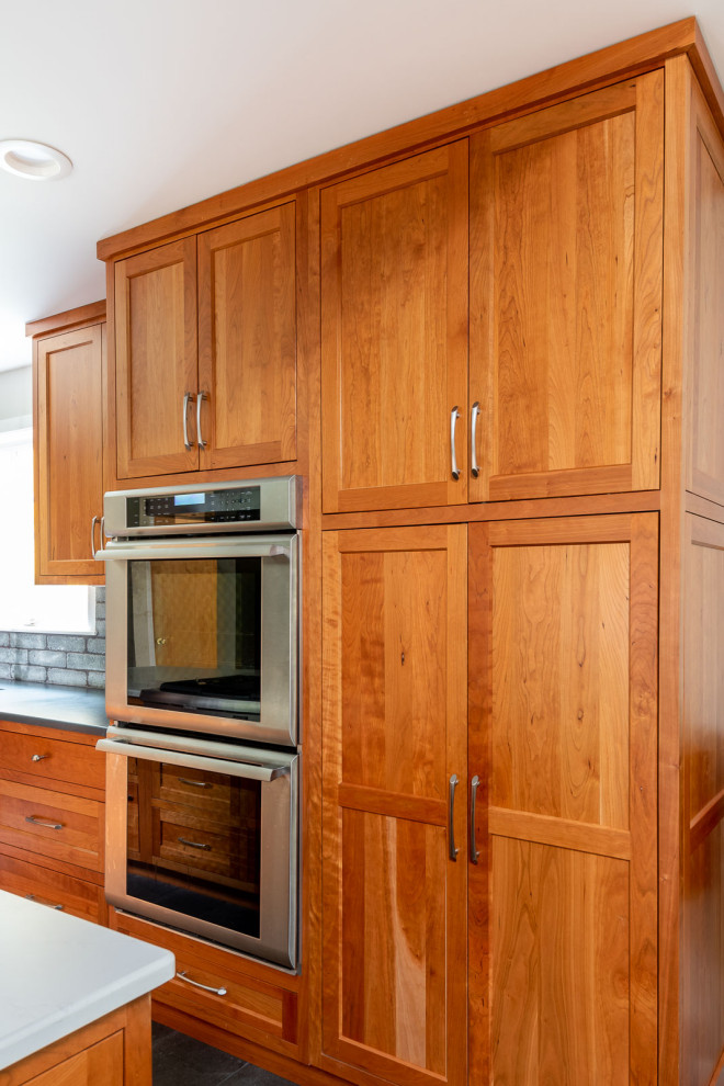 Large transitional l-shaped porcelain tile and gray floor eat-in kitchen photo in Boston with a farmhouse sink, shaker cabinets, medium tone wood cabinets, quartz countertops, gray backsplash, porcelain backsplash, stainless steel appliances, an island and white countertops