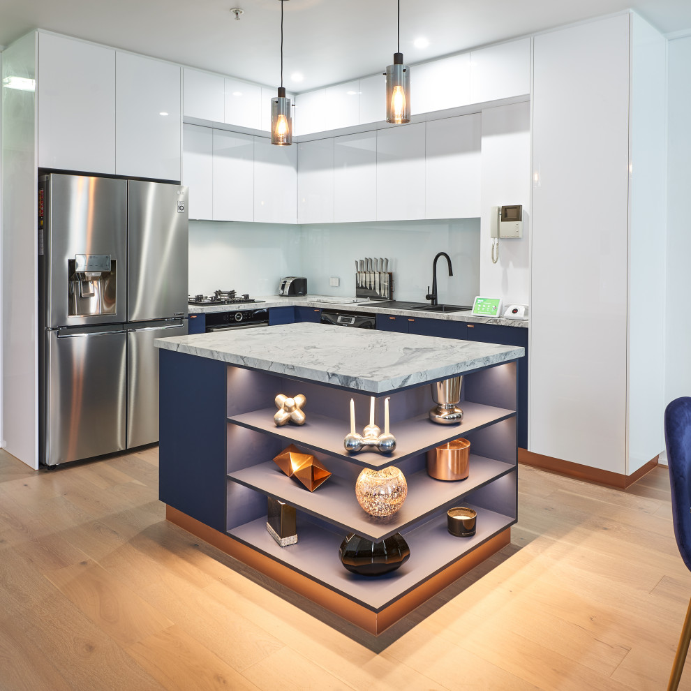 Small contemporary l-shaped kitchen pantry in Melbourne with a drop-in sink, flat-panel cabinets, blue cabinets, quartz benchtops, white splashback, glass sheet splashback, stainless steel appliances, medium hardwood floors, with island, beige floor and white benchtop.