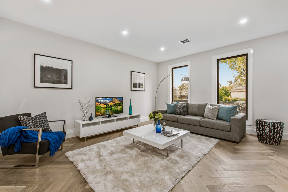 This is an example of a mid-sized contemporary open concept living room in Melbourne with white walls, medium hardwood floors, a freestanding tv and beige floor.