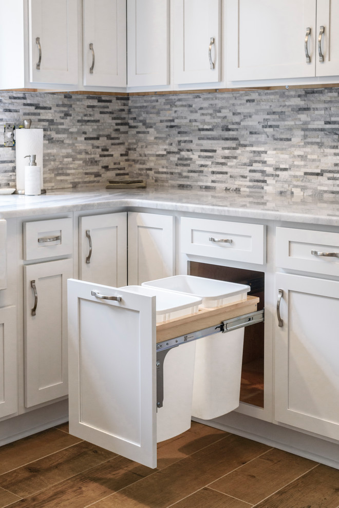 Inspiration for a large transitional l-shaped ceramic tile and brown floor eat-in kitchen remodel in Baltimore with a farmhouse sink, shaker cabinets, white cabinets, granite countertops, gray backsplash, stone tile backsplash, stainless steel appliances, no island and white countertops