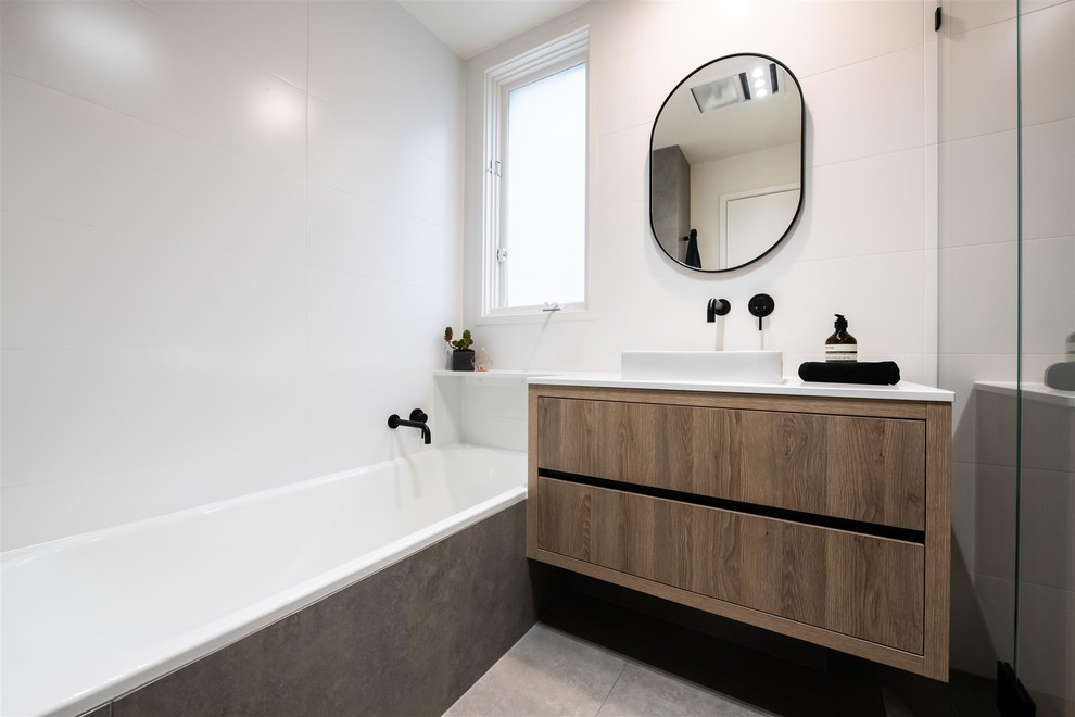 Design ideas for a mid-sized contemporary 3/4 bathroom in Melbourne with furniture-like cabinets, light wood cabinets, a drop-in tub, a one-piece toilet, white tile, ceramic tile, white walls, porcelain floors, a vessel sink, engineered quartz benchtops, grey floor, a hinged shower door and white benchtops.