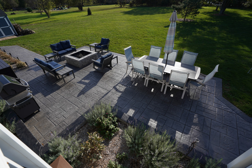 Example of a large minimalist backyard stamped concrete patio design in Detroit with a fire pit and no cover