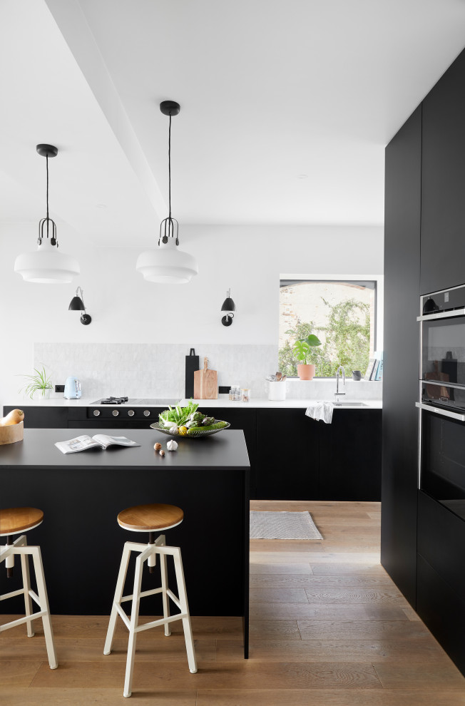 Esempio di un cucina con isola centrale contemporaneo con ante nere, top in superficie solida, paraspruzzi bianco, parquet chiaro e top bianco