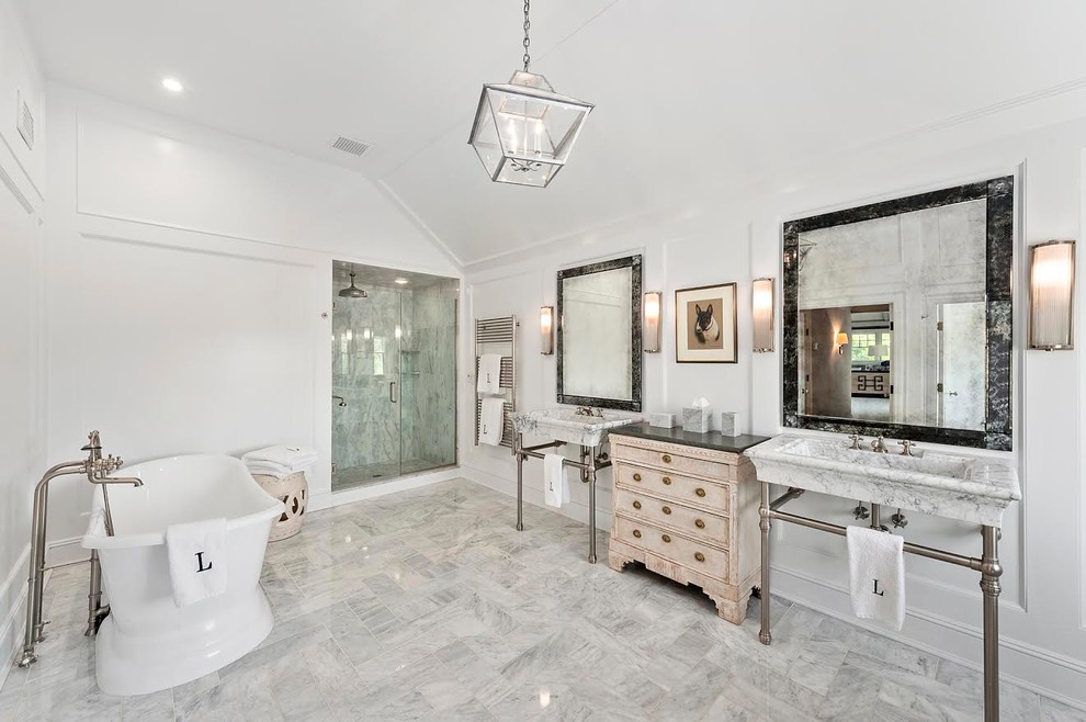 This is an example of a large beach style master bathroom in New York with a freestanding tub, an alcove shower, white tile, white walls, a console sink, white floor, a hinged shower door, marble, marble floors, marble benchtops, distressed cabinets and recessed-panel cabinets.