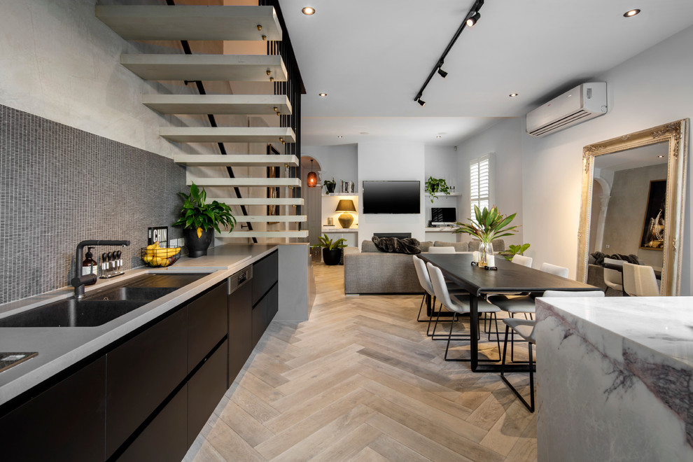 Mid-sized contemporary single-wall open plan kitchen in Melbourne with an undermount sink, black cabinets, marble benchtops, black splashback, mosaic tile splashback, stainless steel appliances, light hardwood floors and with island.