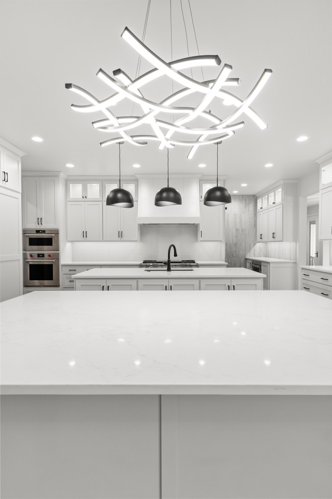 Eat-in kitchen - large transitional u-shaped light wood floor and brown floor eat-in kitchen idea with an undermount sink, shaker cabinets, white cabinets, quartz countertops, white backsplash, porcelain backsplash, stainless steel appliances, two islands and white countertops