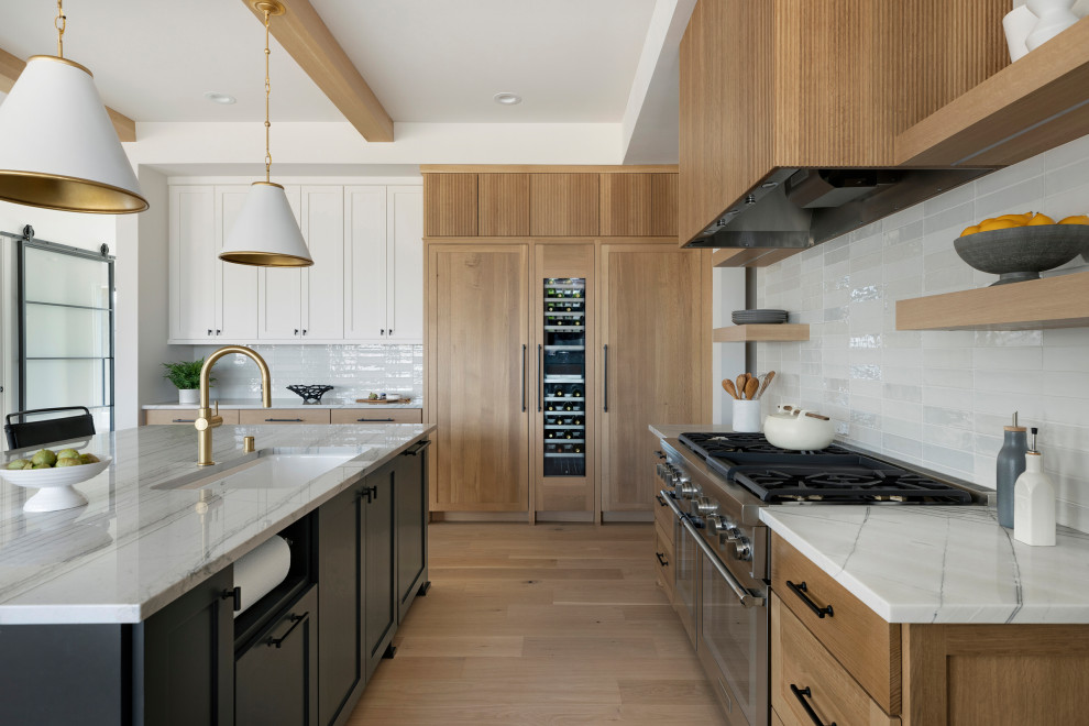 Photo of a modern kitchen in Minneapolis with a drop-in sink, light wood cabinets, quartz benchtops, stainless steel appliances, light hardwood floors, with island and vaulted.