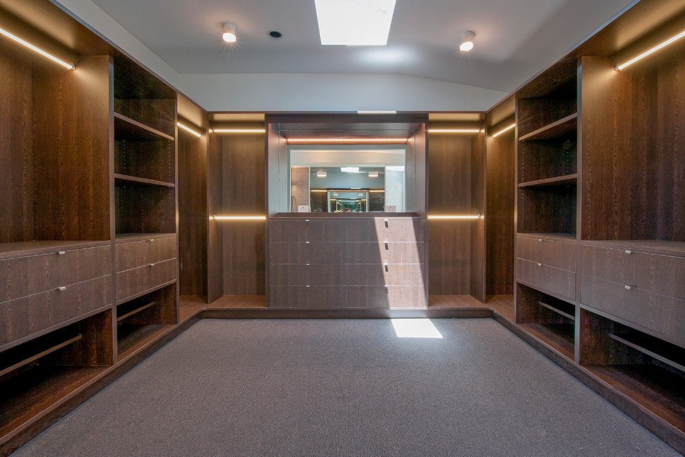 Mid-sized modern gender-neutral dressing room in Melbourne with open cabinets, dark wood cabinets and carpet.
