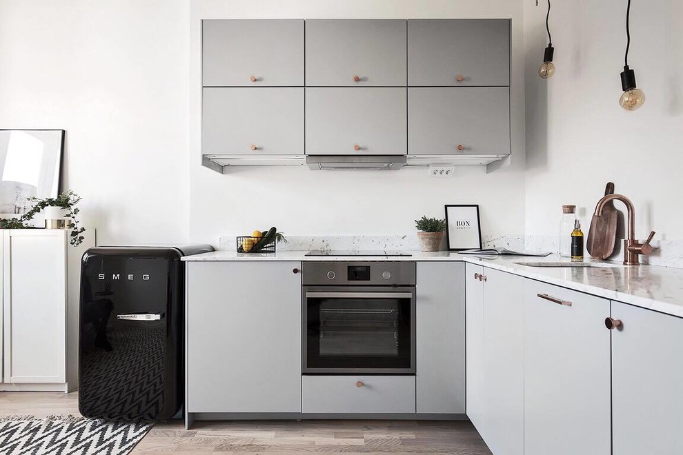 Mid-sized scandinavian l-shaped open plan kitchen in Stockholm with an undermount sink, flat-panel cabinets, grey cabinets, light hardwood floors, no island, marble benchtops and black appliances.