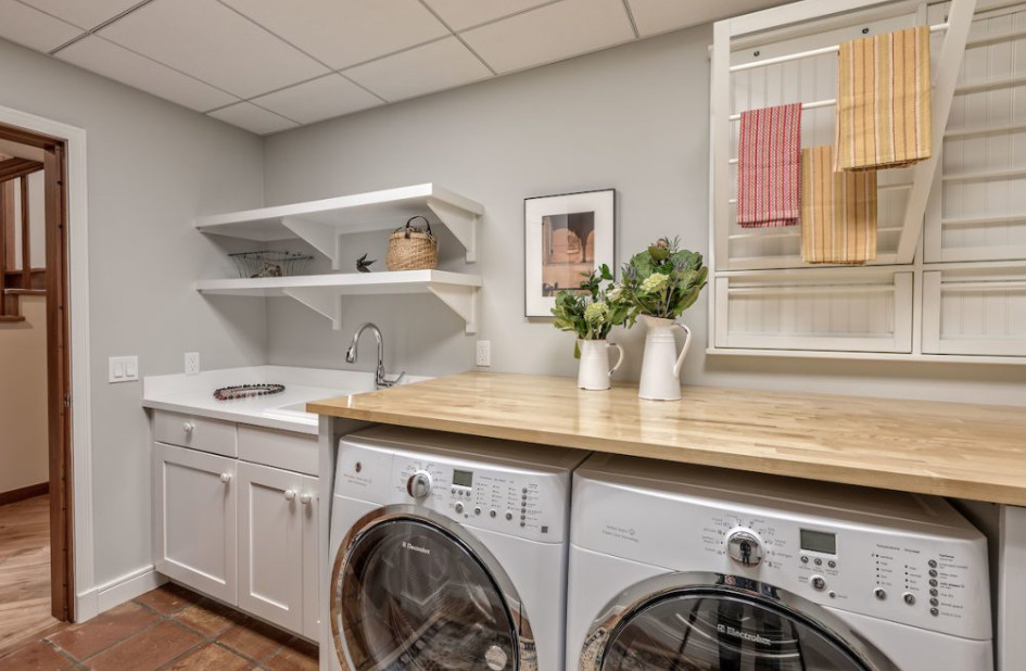 Photo of a mid-sized transitional single-wall dedicated laundry room in Detroit with grey walls, a drop-in sink, shaker cabinets, grey cabinets, wood benchtops, terra-cotta floors, a side-by-side washer and dryer, brown floor and beige benchtop.