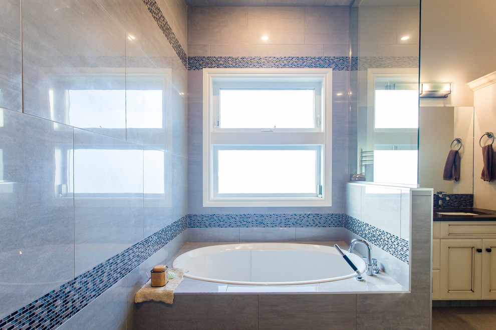 Photo of a mid-sized traditional master bathroom in Calgary with recessed-panel cabinets, a drop-in tub, an alcove shower, a two-piece toilet, multi-coloured tile, glass sheet wall, grey walls, porcelain floors, an undermount sink, engineered quartz benchtops and white cabinets.