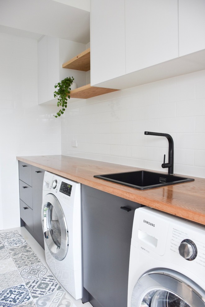 Inspiration for a mid-sized modern dedicated laundry room in Sunshine Coast with a drop-in sink, wood benchtops, white walls, ceramic floors, a side-by-side washer and dryer, white floor and white cabinets.