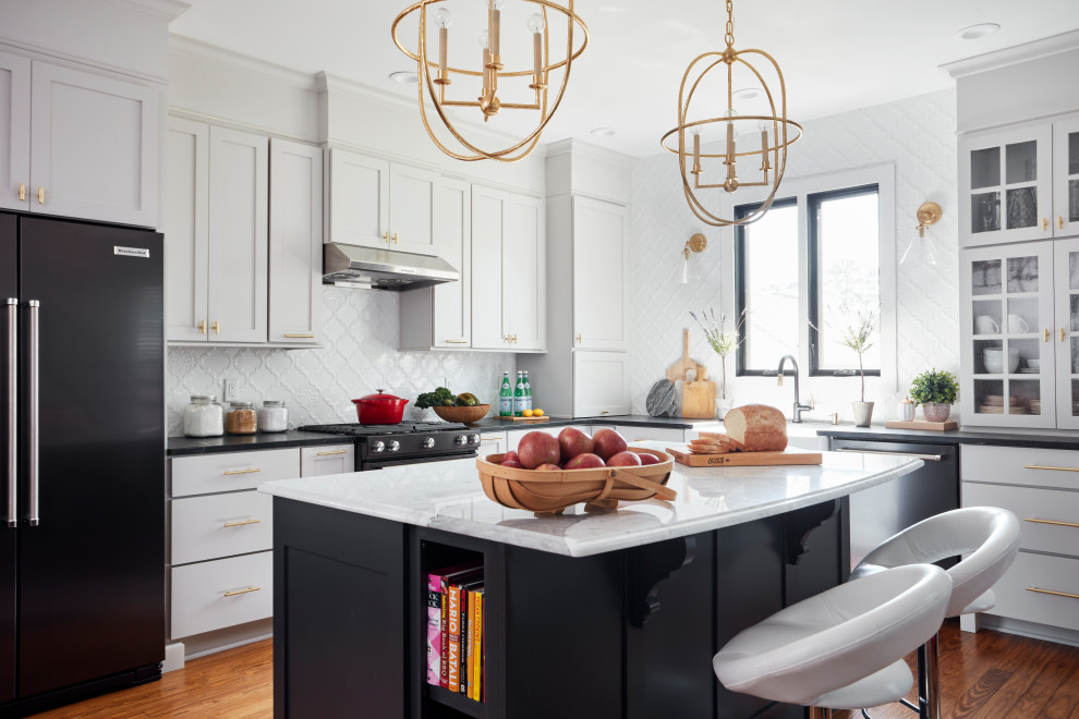 Inspiration for a mid-sized traditional l-shaped eat-in kitchen in St Louis with a farmhouse sink, shaker cabinets, grey cabinets, marble benchtops, white splashback, porcelain splashback, black appliances, medium hardwood floors, with island, brown floor and white benchtop.