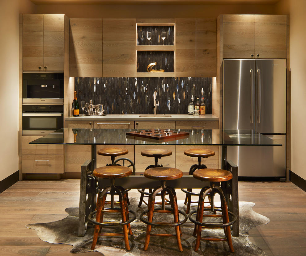 Photo of a large country single-wall wet bar in Denver with an undermount sink, flat-panel cabinets, grey splashback, metal splashback, medium hardwood floors, medium wood cabinets, brown floor, grey benchtop and glass benchtops.
