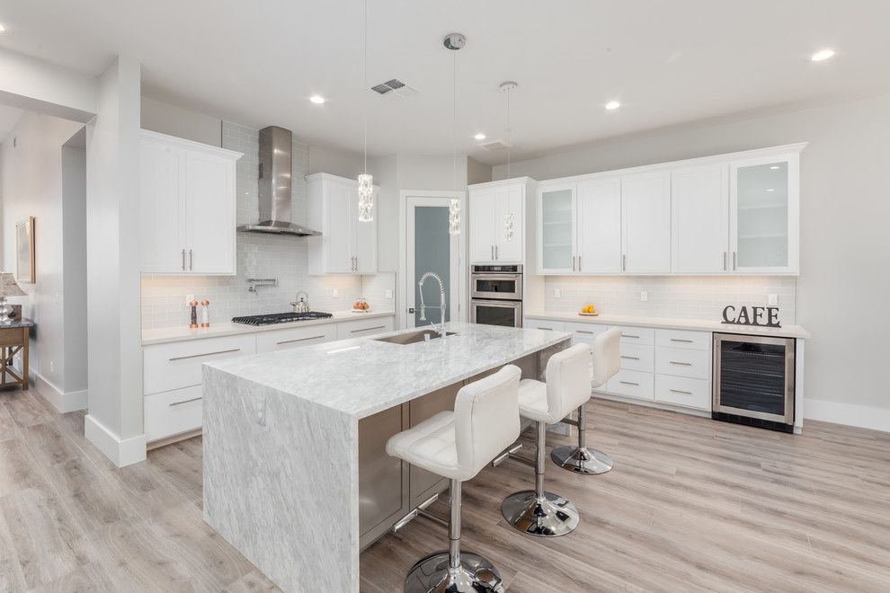 Design ideas for a mid-sized modern l-shaped eat-in kitchen in Sacramento with an integrated sink, flat-panel cabinets, white cabinets, marble benchtops, white splashback, cement tile splashback, stainless steel appliances, light hardwood floors, with island, beige floor and white benchtop.