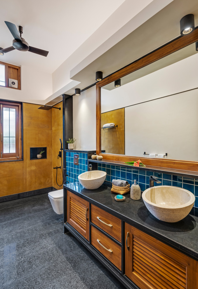 Inredning av ett modernt stort svart svart en-suite badrum, med luckor med lamellpanel, skåp i mellenmörkt trä, en dubbeldusch, en vägghängd toalettstol, blå kakel, keramikplattor, vita väggar, marmorgolv, ett konsol handfat, granitbänkskiva, grått golv och med dusch som är öppen