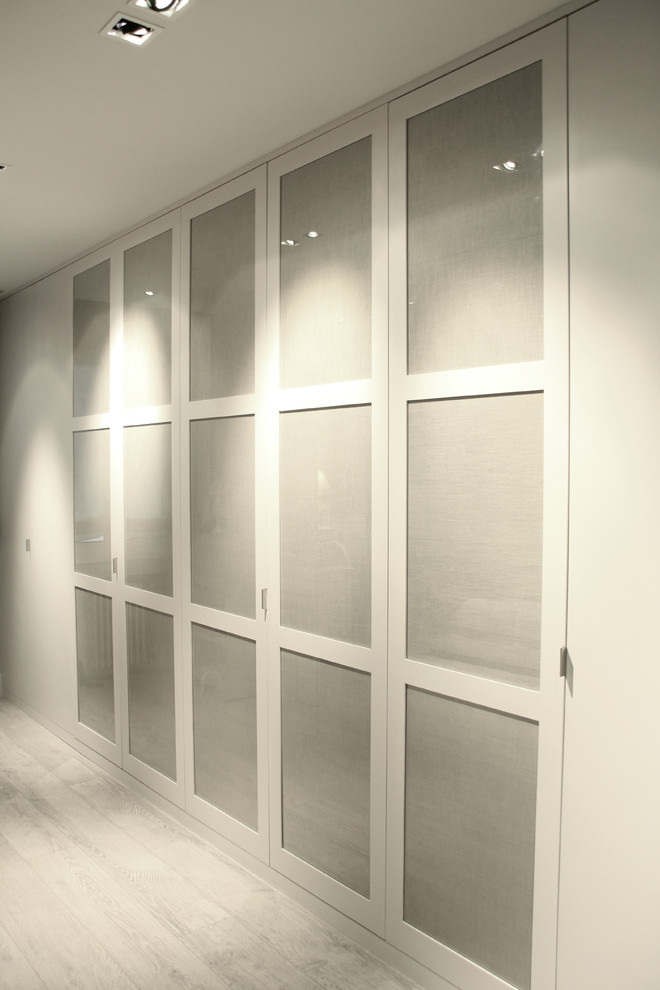 Mid-sized modern gender-neutral built-in wardrobe in Barcelona with glass-front cabinets and white cabinets.