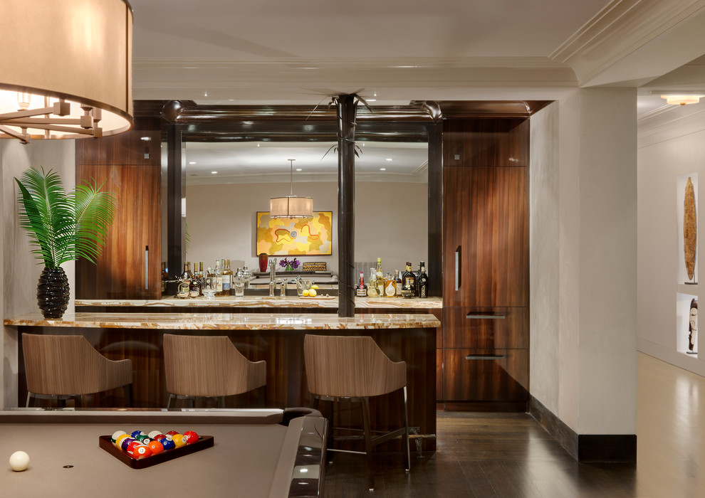 This is an example of a mid-sized transitional galley seated home bar in New York with flat-panel cabinets, dark wood cabinets, onyx benchtops and dark hardwood floors.