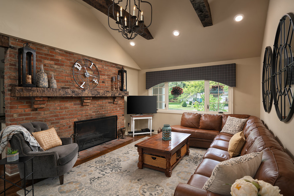 Inspiration for a mid-sized traditional enclosed family room in Columbus with beige walls, medium hardwood floors, a standard fireplace, a brick fireplace surround, a freestanding tv and brown floor.