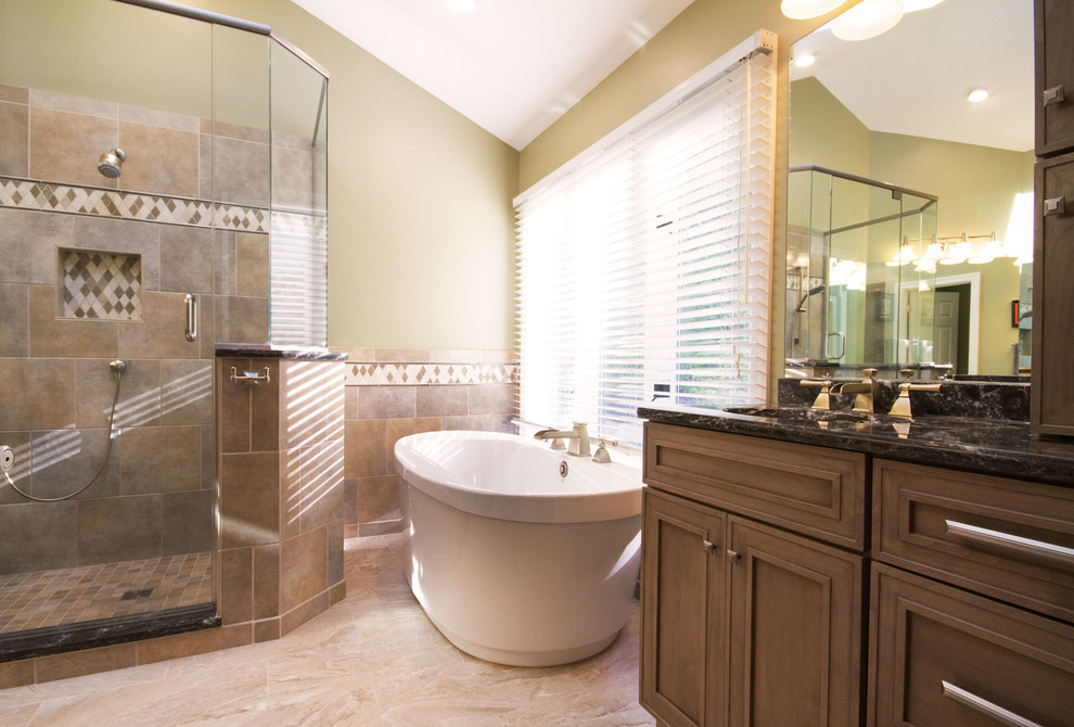 Design ideas for a large traditional master bathroom in St Louis with beaded inset cabinets, medium wood cabinets, a freestanding tub, a double shower, beige tile, ceramic tile, beige walls, limestone floors, an undermount sink, granite benchtops, beige floor and a hinged shower door.