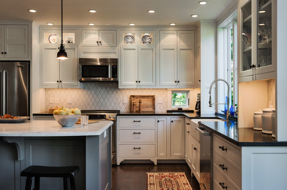 This is an example of a beach style l-shaped eat-in kitchen in Portland Maine with a farmhouse sink, beaded inset cabinets, white cabinets, white splashback, stone tile splashback, stainless steel appliances and granite benchtops.
