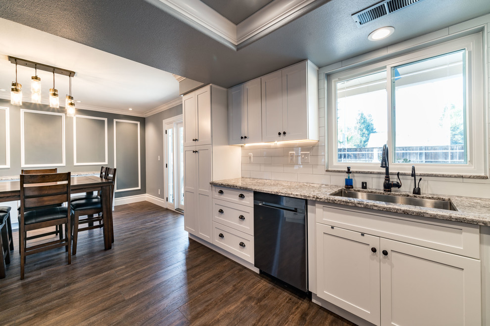 Mid-sized transitional u-shaped dark wood floor and brown floor eat-in kitchen photo with an undermount sink, shaker cabinets, white cabinets, granite countertops, white backsplash, subway tile backsplash, stainless steel appliances and an island