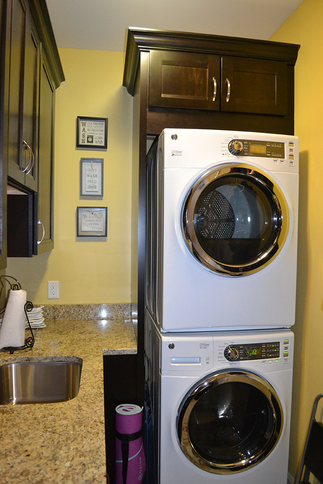 コロンバスにある小さなトランジショナルスタイルのおしゃれな洗濯室 (L型、アンダーカウンターシンク、落し込みパネル扉のキャビネット、濃色木目調キャビネット、御影石カウンター、黄色い壁、上下配置の洗濯機・乾燥機) の写真