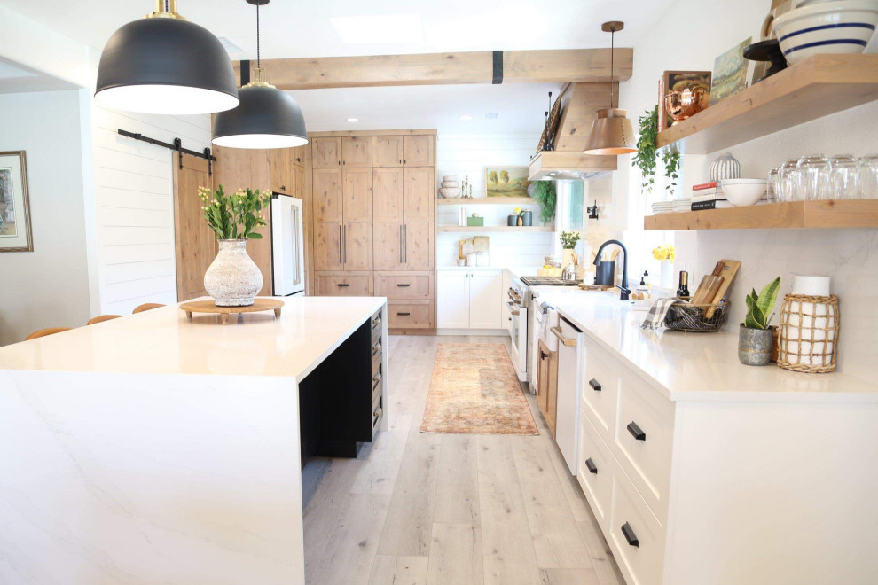 This is an example of a large modern single-wall eat-in kitchen in Other with a farmhouse sink, shaker cabinets, white cabinets, quartz benchtops, white splashback, engineered quartz splashback, white appliances, laminate floors, with island, grey floor, white benchtop and exposed beam.