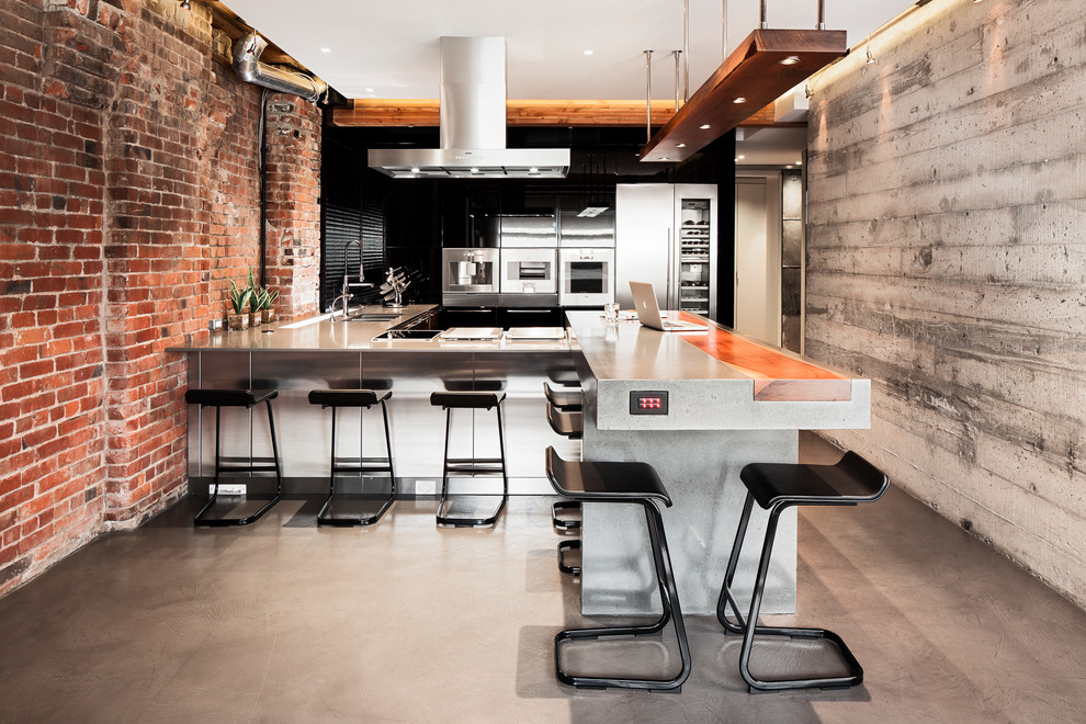 Design ideas for a large industrial u-shaped open plan kitchen in Vancouver with concrete benchtops, stainless steel appliances, concrete floors, flat-panel cabinets, black splashback, a peninsula and black cabinets.