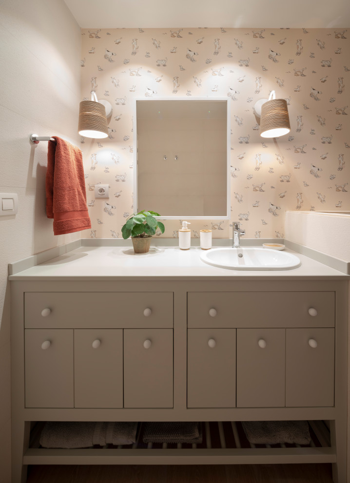This is an example of a mid-sized transitional kids bathroom in Bilbao with furniture-like cabinets, white cabinets, an alcove tub, a wall-mount toilet, beige tile, wood-look tile, beige walls, wood-look tile, an undermount sink, wood benchtops, brown floor, grey benchtops, an enclosed toilet, a single vanity, a built-in vanity, recessed and wallpaper.