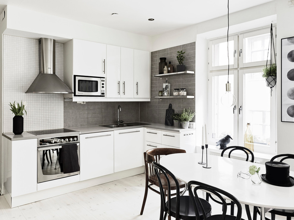This is an example of a mid-sized scandinavian l-shaped eat-in kitchen in Gothenburg with a double-bowl sink, flat-panel cabinets, white cabinets, grey splashback, stainless steel appliances, light hardwood floors and no island.