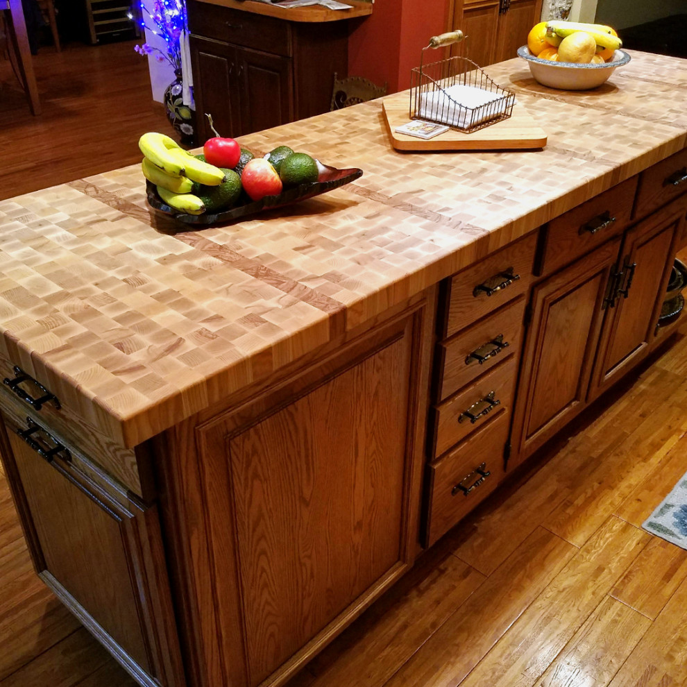 This is an example of a large country l-shaped eat-in kitchen in Other with raised-panel cabinets, brown cabinets, wood benchtops, medium hardwood floors, with island, brown floor and yellow benchtop.