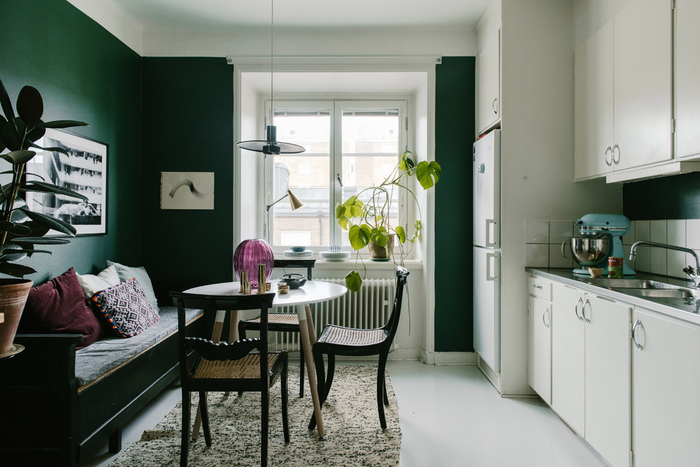 Mid-sized transitional single-wall eat-in kitchen in Stockholm with a double-bowl sink, flat-panel cabinets, white cabinets, stainless steel benchtops, white splashback, ceramic splashback, white appliances, linoleum floors, grey floor and no island.