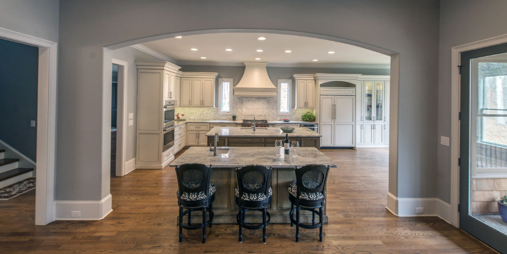Example of a large transitional l-shaped medium tone wood floor and brown floor eat-in kitchen design with an undermount sink, gray backsplash, stainless steel appliances, two islands, beige cabinets, marble countertops and glass tile backsplash
