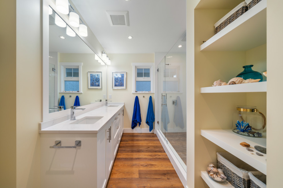 This is an example of a mid-sized beach style master bathroom in Vancouver with shaker cabinets, white cabinets, white tile, white walls, medium hardwood floors, an undermount sink, engineered quartz benchtops, brown floor, a hinged shower door, white benchtops, a niche, a double vanity and a built-in vanity.