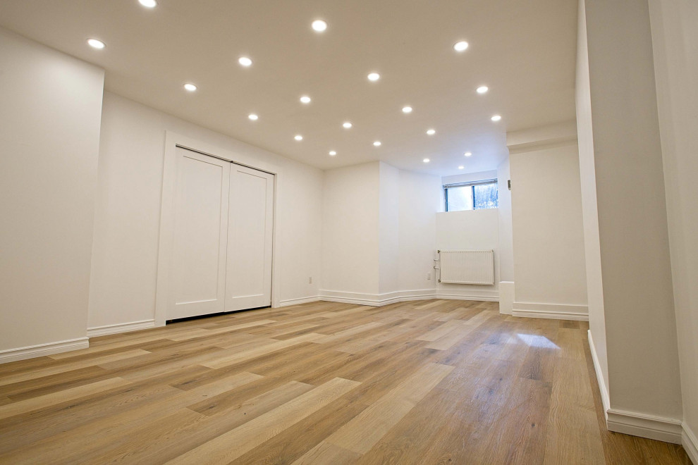 Medium sized modern fully buried basement in Toronto with a game room, white walls, vinyl flooring and brown floors.