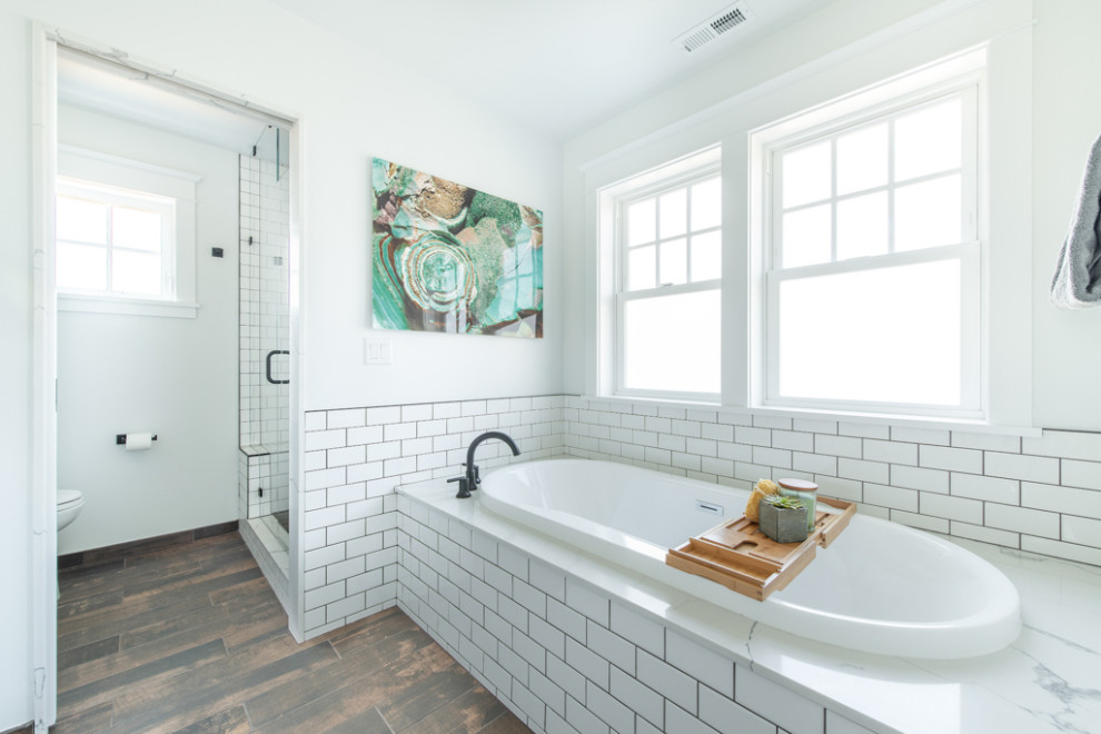 Photo of a large arts and crafts master bathroom in Seattle with shaker cabinets, white cabinets, a drop-in tub, an alcove shower, a two-piece toilet, white tile, ceramic tile, white walls, porcelain floors, a drop-in sink, engineered quartz benchtops, brown floor, a hinged shower door, white benchtops, an enclosed toilet, a double vanity and a built-in vanity.