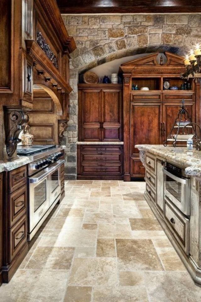 Example of a large mountain style single-wall travertine floor and beige floor enclosed kitchen design in Orange County with an undermount sink, raised-panel cabinets, dark wood cabinets, granite countertops, stainless steel appliances and an island