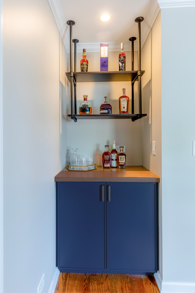 This is an example of a mid-sized transitional home bar in Chicago with blue cabinets, wood benchtops and light hardwood floors.