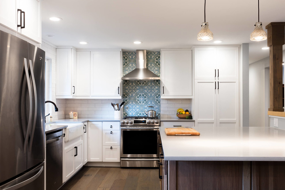 Transitional l-shaped kitchen in Seattle with a farmhouse sink, shaker cabinets, white cabinets, blue splashback, cement tile splashback, stainless steel appliances, dark hardwood floors, with island and brown floor.