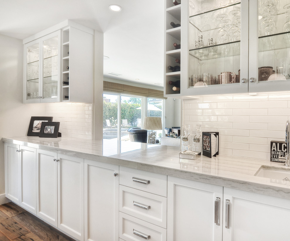 Inspiration for a mid-sized transitional l-shaped medium tone wood floor and brown floor kitchen remodel in Orange County with an undermount sink, recessed-panel cabinets, white cabinets, white backsplash, stainless steel appliances, an island, subway tile backsplash, white countertops and quartzite countertops