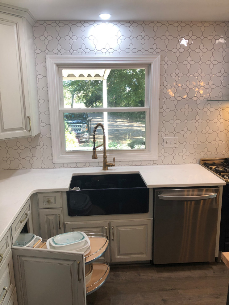 Mid-sized transitional l-shaped vinyl floor and brown floor kitchen photo in DC Metro with a farmhouse sink, raised-panel cabinets, gray cabinets, solid surface countertops, white backsplash, ceramic backsplash, stainless steel appliances, an island and white countertops