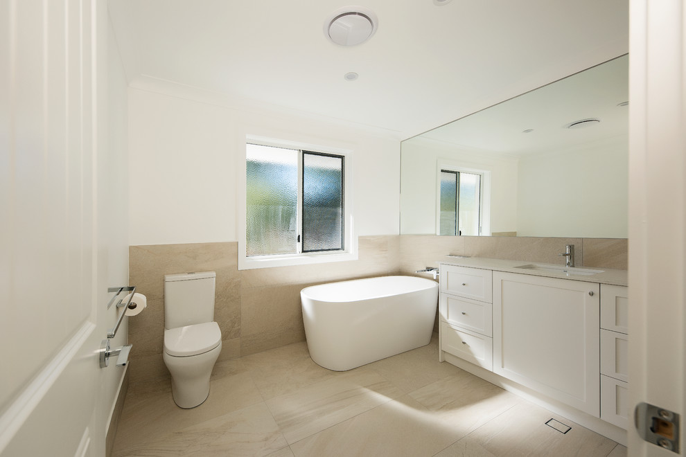 Mid-sized contemporary bathroom in Brisbane with beaded inset cabinets, white cabinets, a freestanding tub, an alcove shower, a two-piece toilet, beige tile, travertine, white walls, travertine floors, an undermount sink, marble benchtops, beige floor and a hinged shower door.