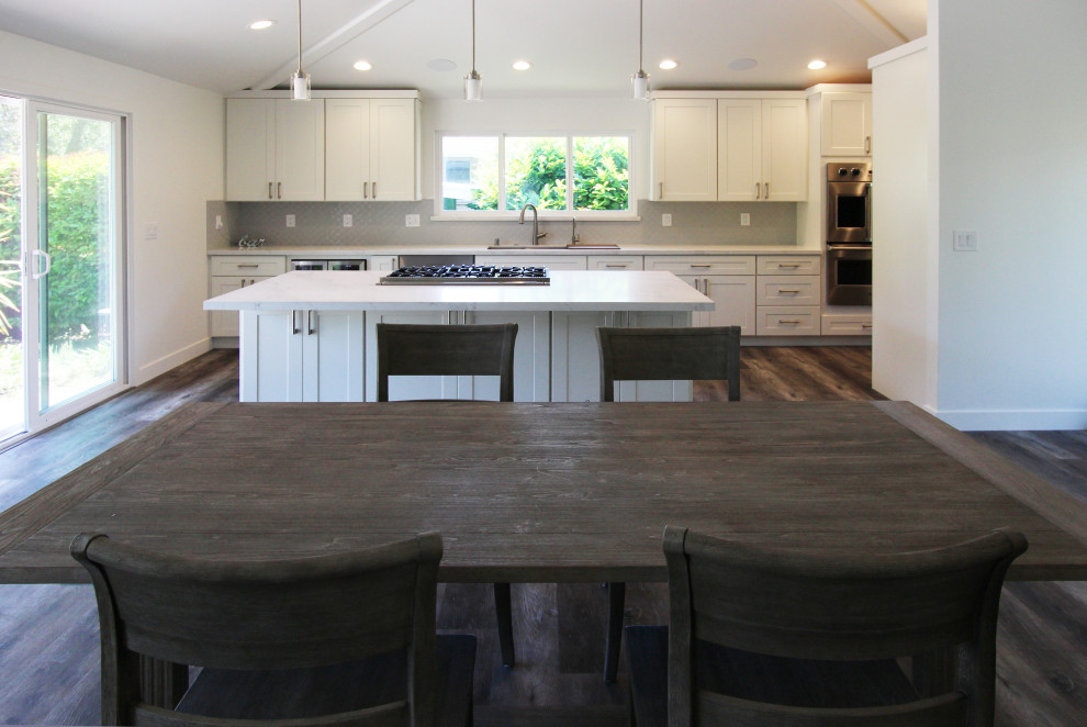 Example of a large transitional single-wall vinyl floor and brown floor open concept kitchen design with an undermount sink, shaker cabinets, white cabinets, quartz countertops, gray backsplash, ceramic backsplash, stainless steel appliances, an island and white countertops
