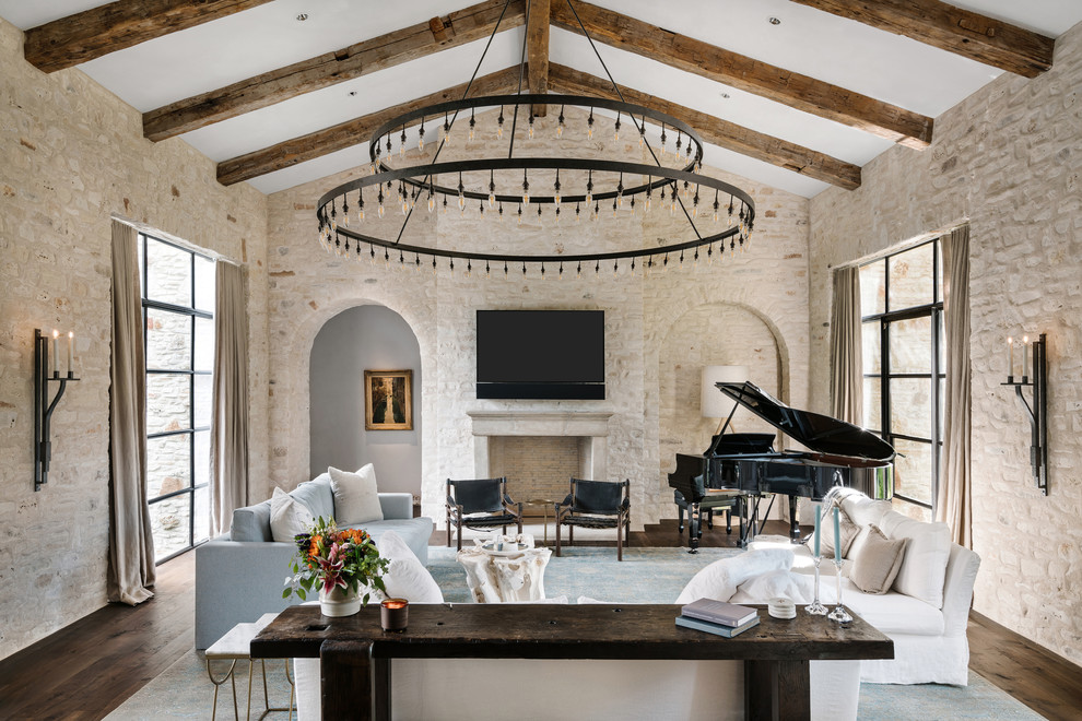 Photo of a mediterranean family room in Austin with a music area, beige walls, dark hardwood floors, a standard fireplace and a wall-mounted tv.