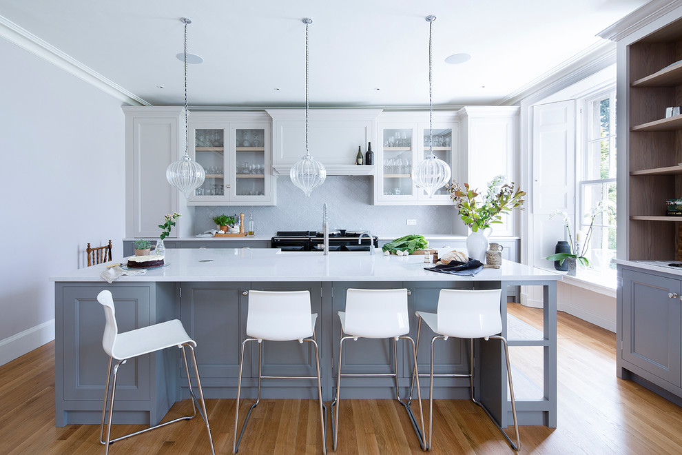 Inspiration for a transitional kitchen in Other with quartz benchtops, grey cabinets, beige floor, glass-front cabinets, grey splashback, black appliances, light hardwood floors and with island.